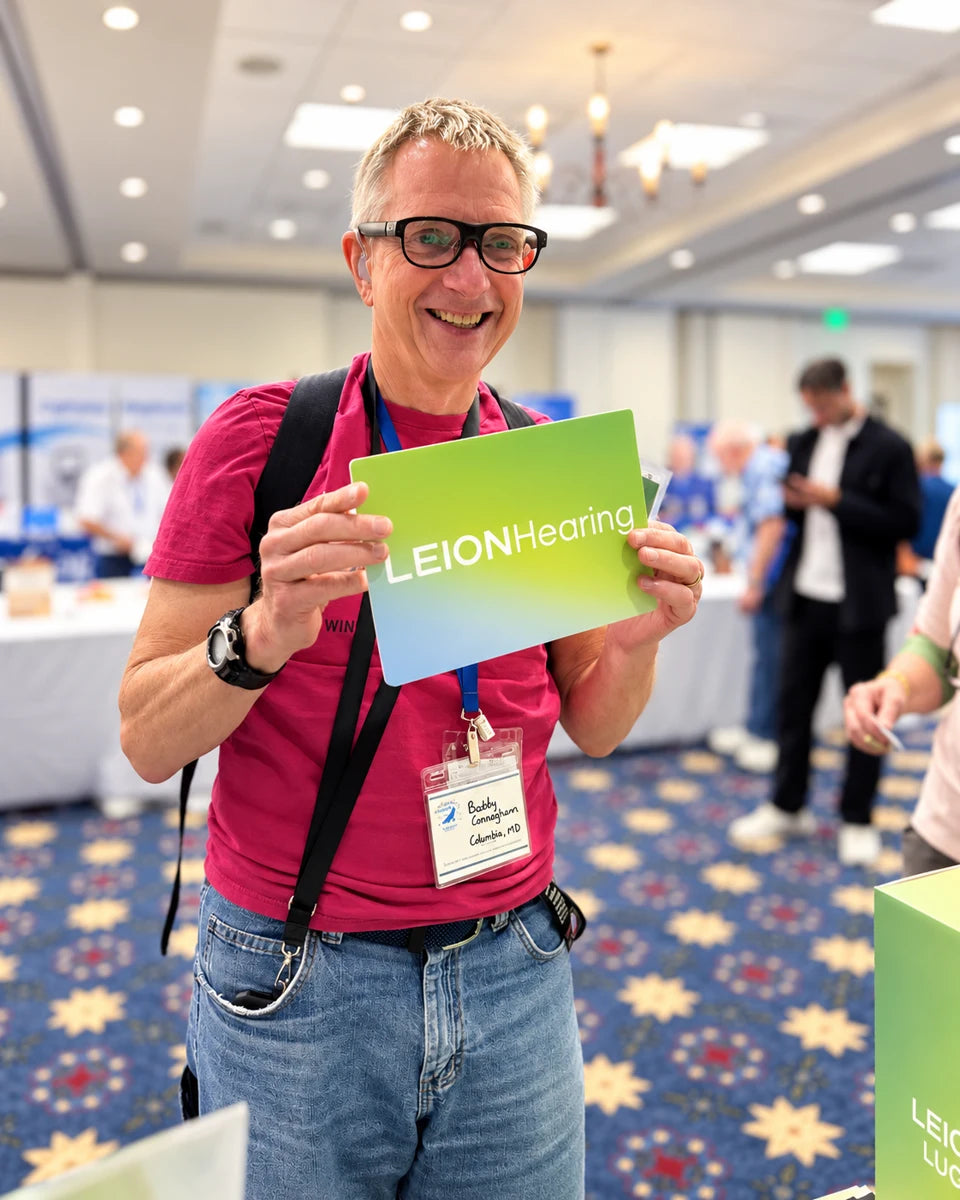 ALDAcon attendee wearing caption glasses and holding a LEION Hearing sign